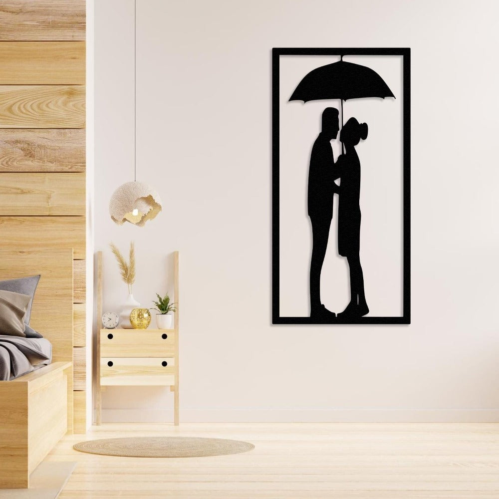Black metal wall art of a couple under an umbrella, displayed in a cozy bedroom with light wooden furniture and minimalist decor.