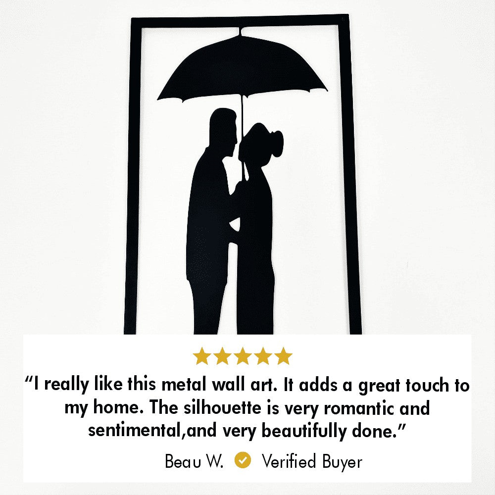 Close-up of a black framed metal wall art depicting a couple under an umbrella.