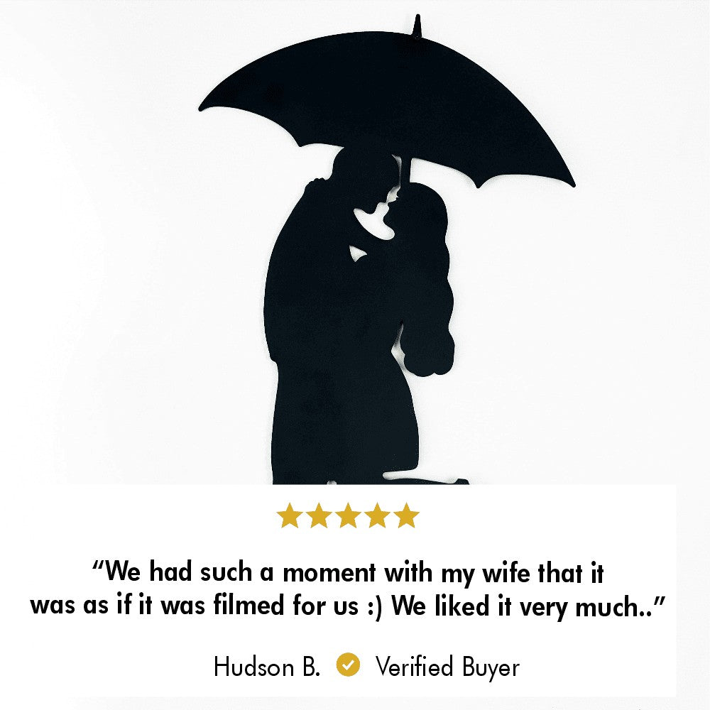 A close-up view of a black metal wall art featuring a couple embracing under an umbrella.