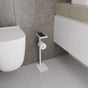A white floor-mounted toilet paper holder with a built-in shelf, styled in a bathroom with light gray tiles and minimalist decor.