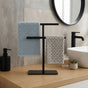 Black freestanding countertop towel holder with blue and gray towels on a modern bathroom vanity.