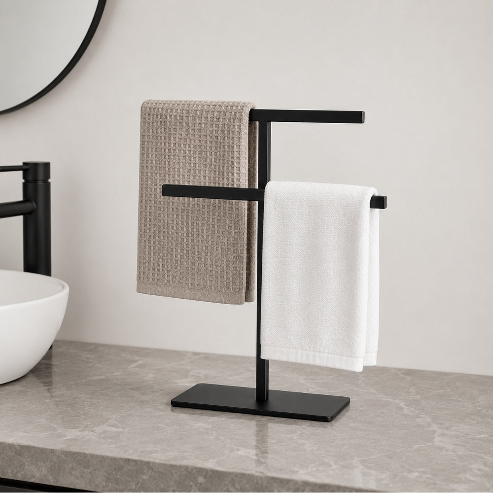 Black freestanding countertop towel holder with folded towels on a bathroom counter.
