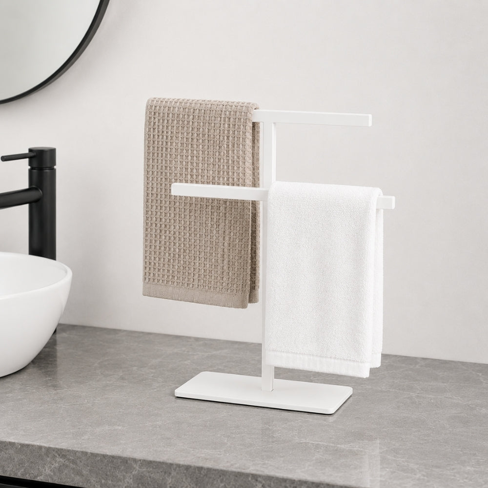 White freestanding countertop towel holder with towels on a light bathroom counter.