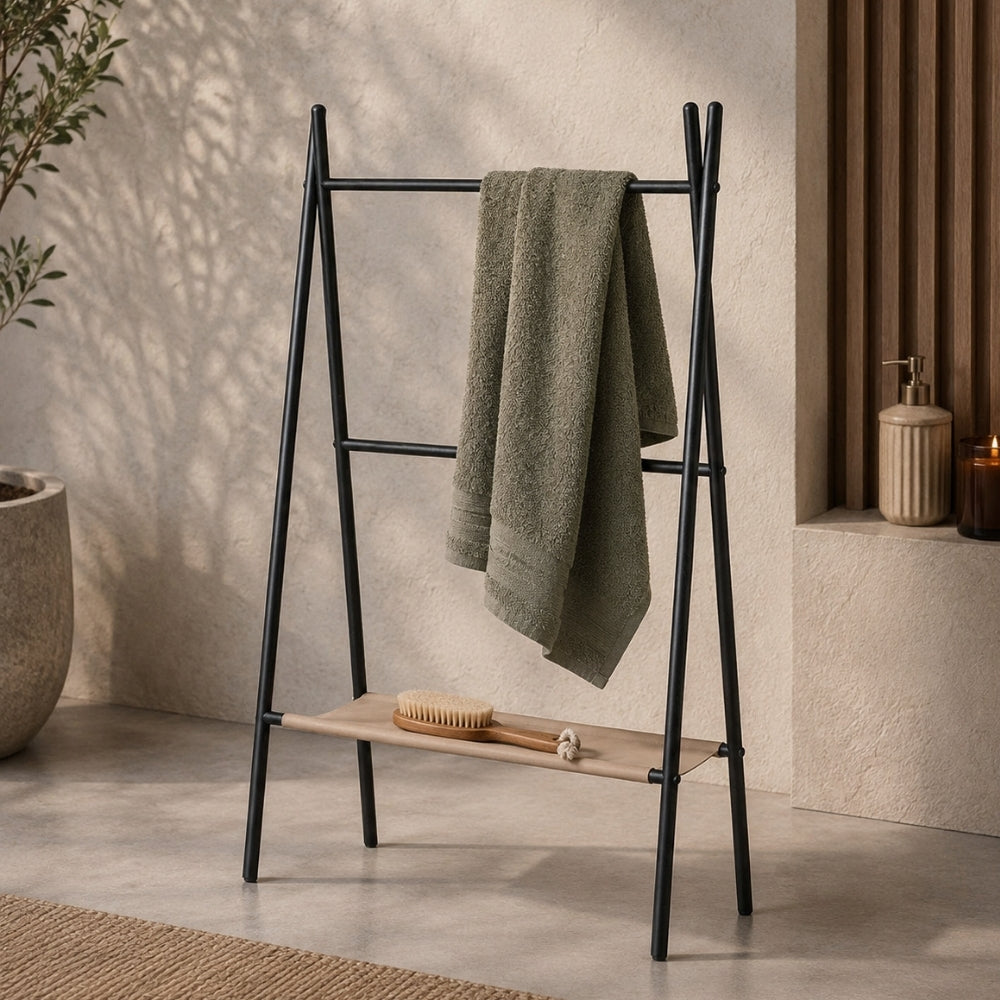 Black freestanding ladder towel rack with shelf holding a green towel in a warm bathroom scene.