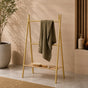 Gold freestanding ladder towel rack with shelf holding a green towel in a warm bathroom scene.