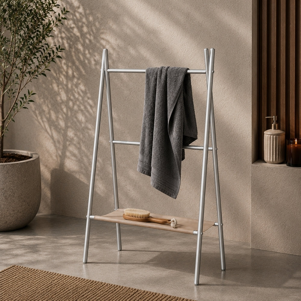 Satin nickel freestanding ladder towel rack with shelf holding a gray towel in a warm bathroom scene.