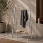 Satin nickel freestanding ladder towel rack with shelf holding a gray towel in a warm bathroom scene.