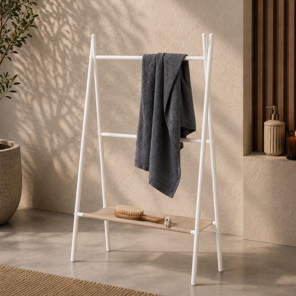 White freestanding ladder towel rack with shelf holding a gray towel in a warm bathroom scene.
