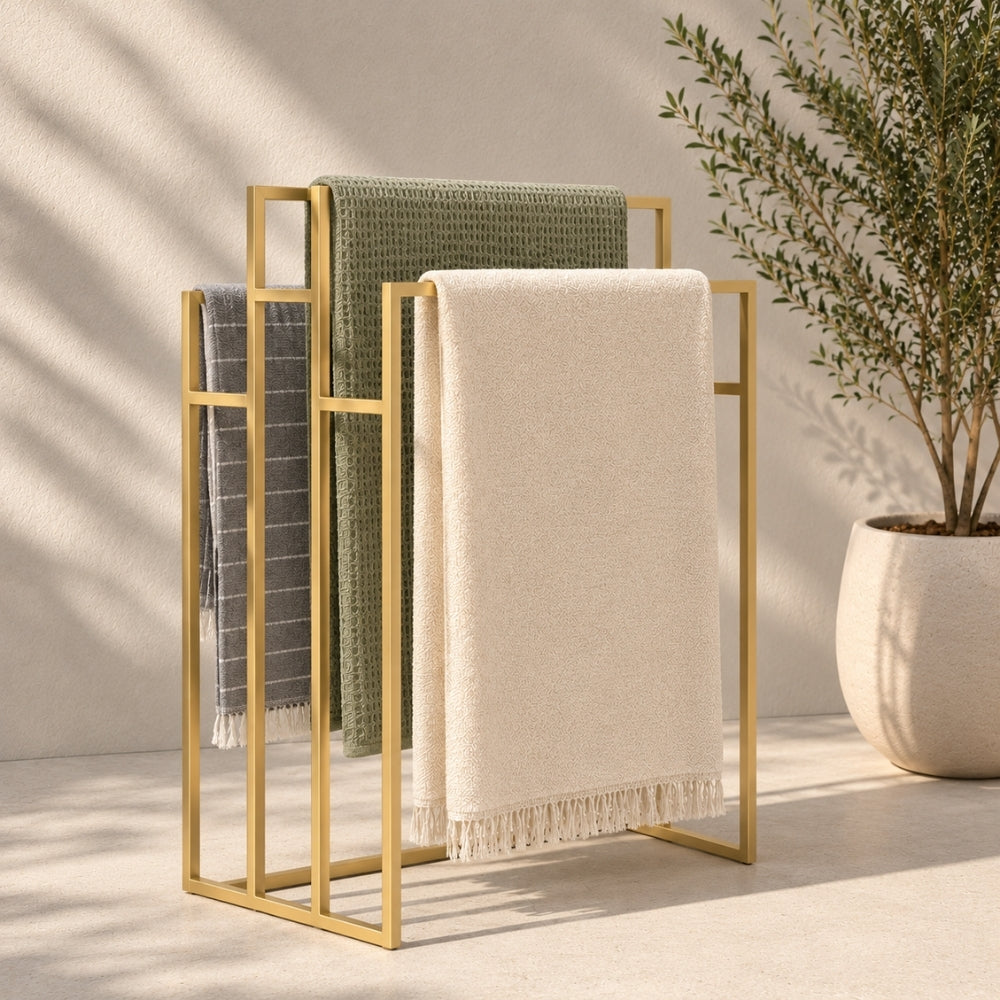 Gold freestanding outdoor pool towel rack with multiple towels hanging on separate rails.