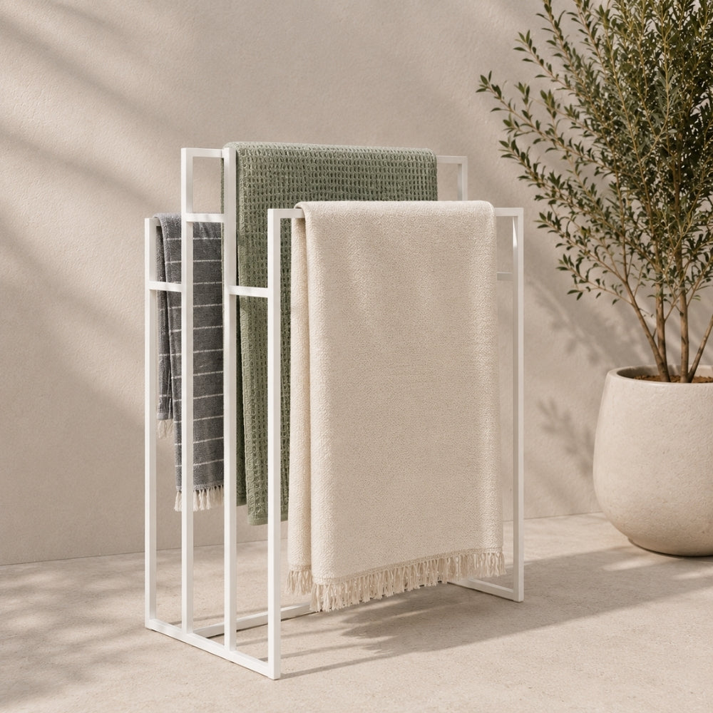 White freestanding outdoor pool towel rack with multiple towels hanging on separate rails.