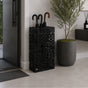 Black geometric lattice metal umbrella stand in modern entryway with olive plant and console table