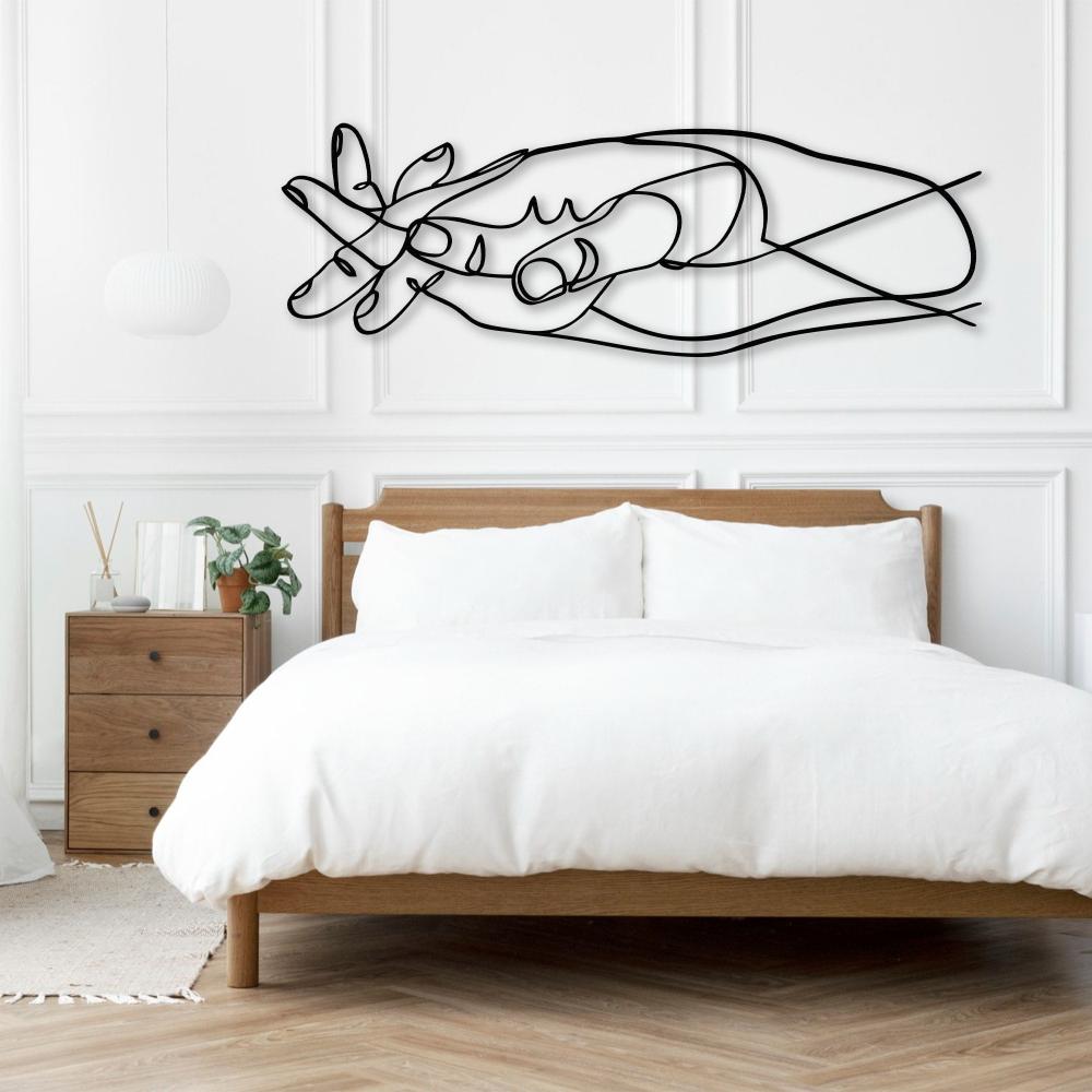 Metal wall art of intertwined hands mounted above a minimalist wooden bed with white bedding in a bright bedroom.
