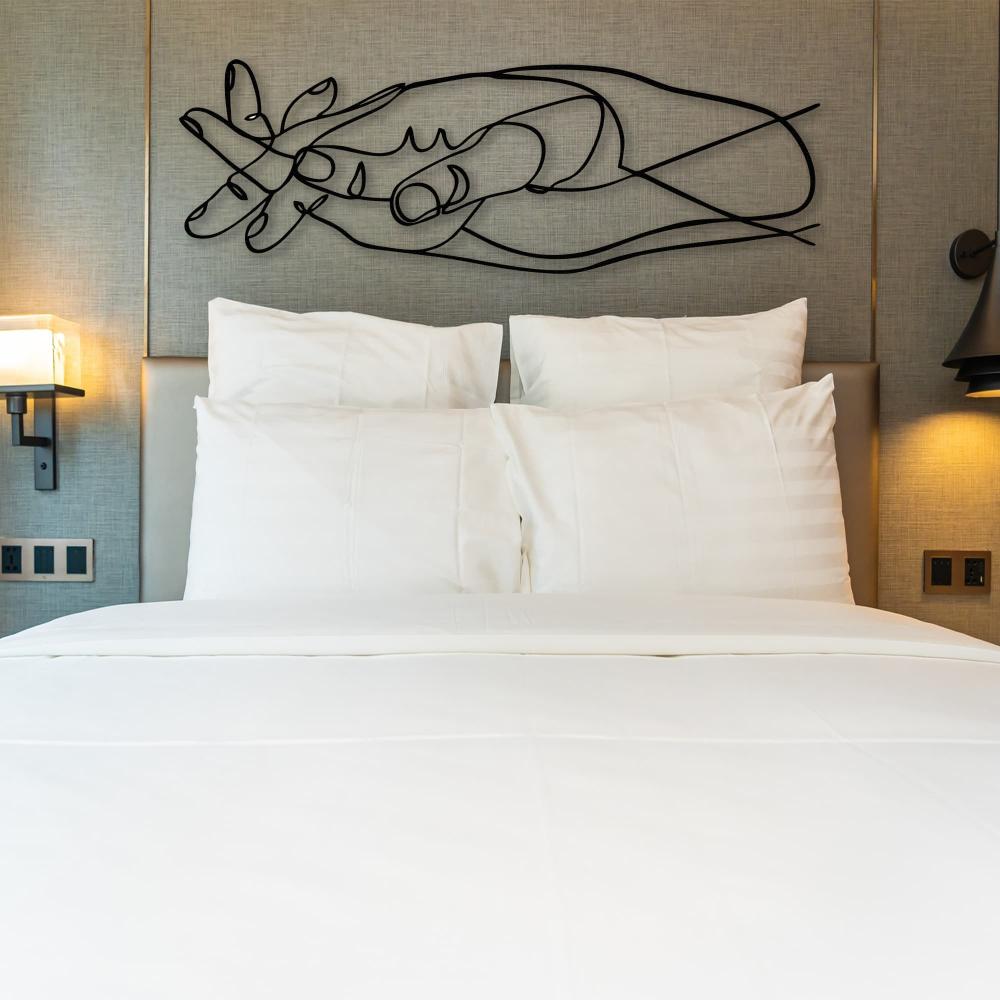 Intertwined hands modern metal wall art displayed above a hotel bed with modern lighting and white bedding.