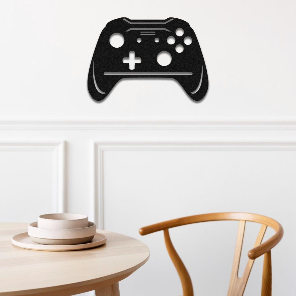 Black joystick-shaped metal wall art mounted on a white paneled wall, situated above a minimalist wooden dining table with stacked neutral-toned bowls and a matching wooden chair, combining gaming with modern decor.