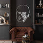 A white metal wall decor of a man's face with floral and leaf elements, mounted on a dark wall in a classic library room with a brown leather armchair and decorative bookshelf. 