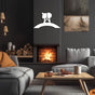 White metal wall art of a couple on a bridge, mounted on a dark wall above a cozy fireplace in a modern living room setting.