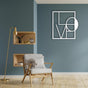 A modern room with white metal "LOVE" wall art in a geometric design, mounted on a blue wall with minimalistic decor including a wooden shelf and gold accents.
