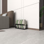 A modern black Metal Slippers and Shoe Rack neatly holding three pairs of slippers in a contemporary living room with a beige armchair.