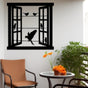 Metal wall art depicting an open window with birds perched on wires and one bird in mid-flight, displayed in a cozy balcony setting with a round table, chair, and vibrant flowers.