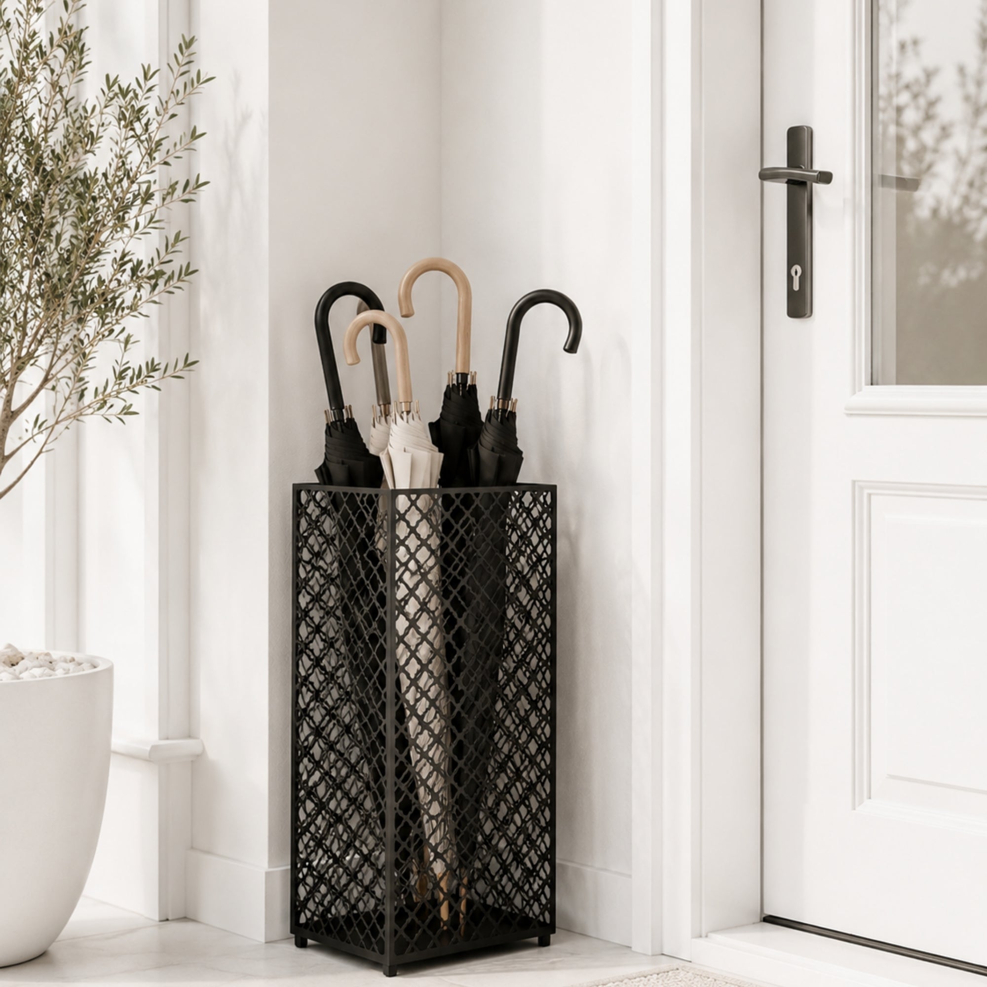 Black mesh metal umbrella stand at modern front door with multi-color umbrellas and olive plant