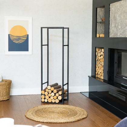 Modern Indoor Log Holder in Black, shown beside a wall fireplace with stacked logs and framed art in a contemporary living room.