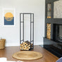 Modern Indoor Log Holder in Black, shown beside a wall fireplace with stacked logs and framed art in a contemporary living room.