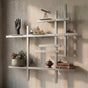 Satin nickel modular metal wall shelf with books, plants, and decorative objects on a textured wall.