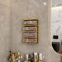 Gold wall-mounted towel rack in a stylish bathroom, holding neatly rolled beige towels. The luxurious golden finish stands out against the neutral-toned tile wall, enhancing the elegant decor. Below the rack, a collection of spa essentials and dried flowers adds a touch of sophistication and practicality