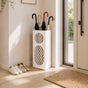 White oval mesh metal umbrella stand in sunlit modern entryway with shoes on wooden floor