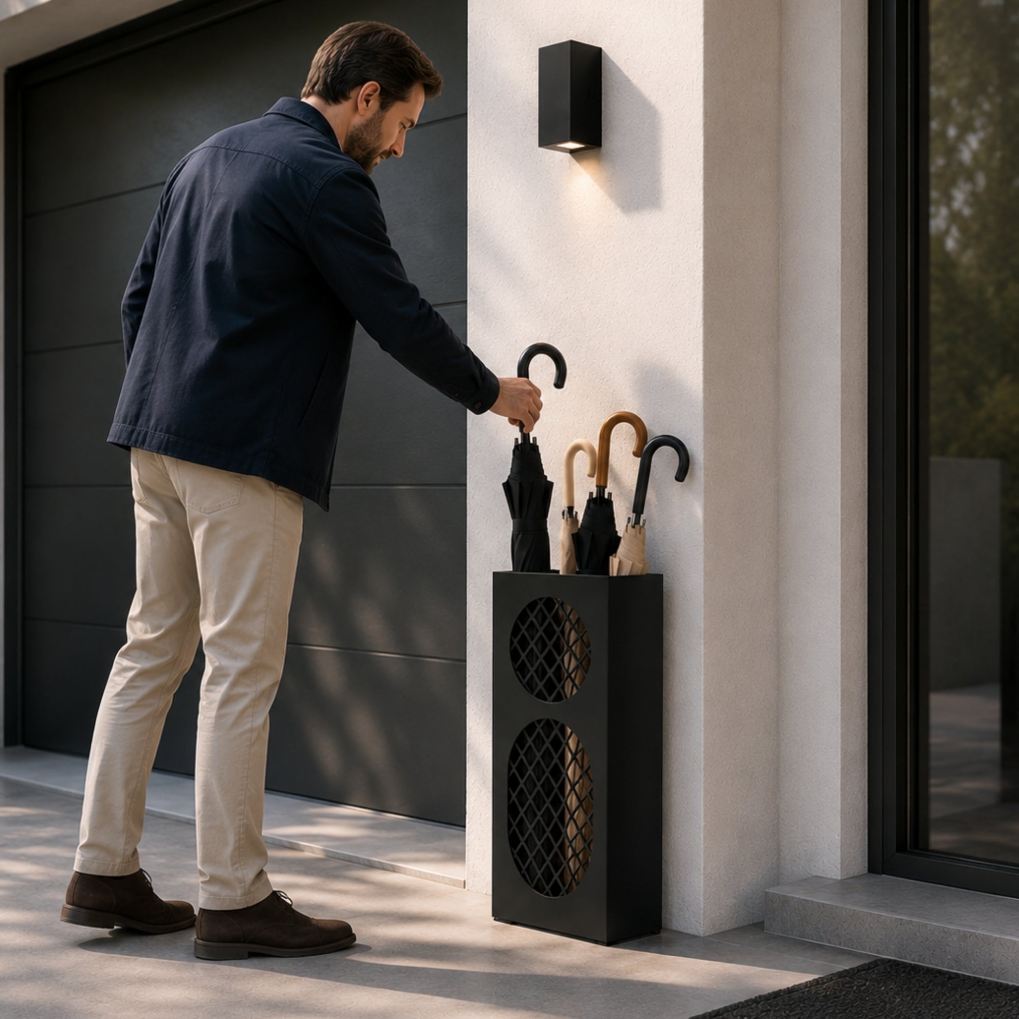 Man in navy jacket placing umbrella in black oval mesh metal umbrella stand at modern entrance