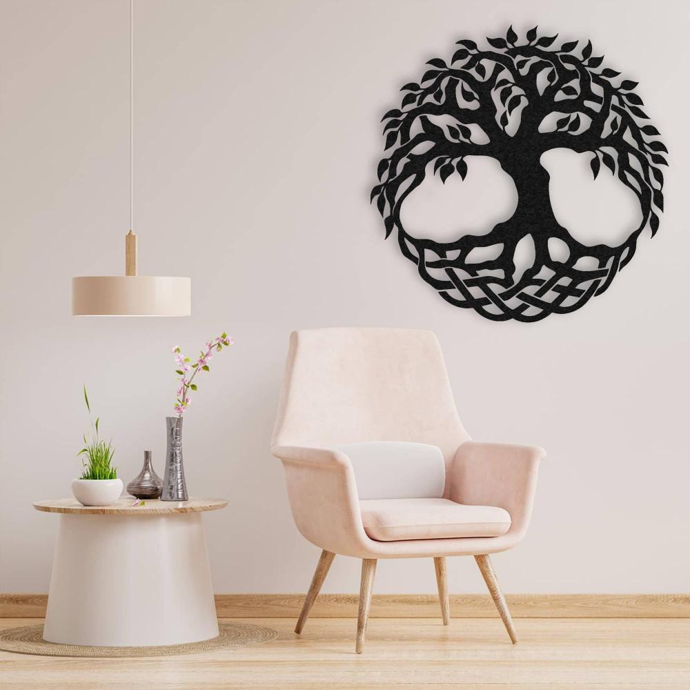 Black metal tree of life wall art featuring intricate branches and a Celtic-inspired base design, elegantly displayed above a pastel pink armchair and a minimalist round side table in a cozy, modern living space.