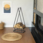Wooden logs in a metal stand next to a fireplace in a room with a woven mat on the floor. pine tree shaped firewood rack, decorative firewood rack indoor outdoor