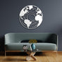 Round earth-themed metal wall art in a white concentric map design, mounted on a dark gray wall above a modern green sofa. The room features wooden flooring, a stylish glass coffee table with decorative elements, and a minimalist aesthetic.
