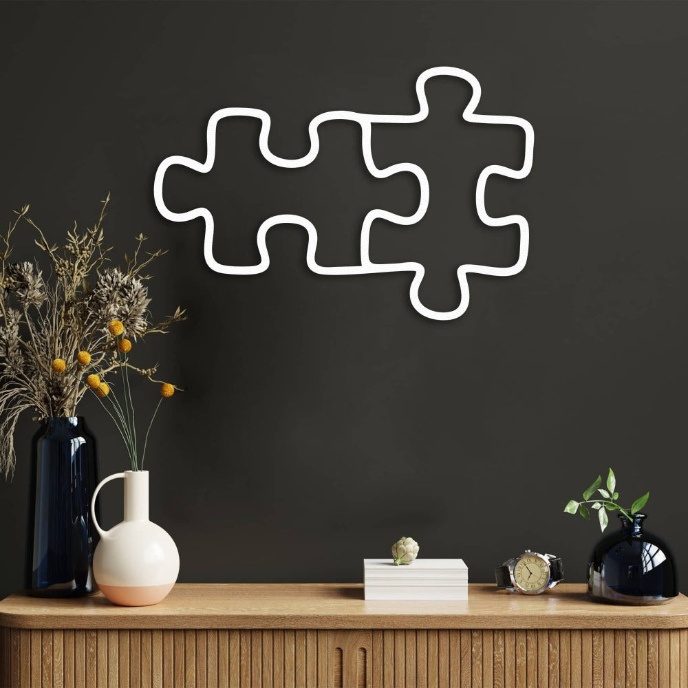 Two connected white puzzle piece metal wall art placed above a wooden console table with vases and modern decor items, adding a clean and contemporary touch.