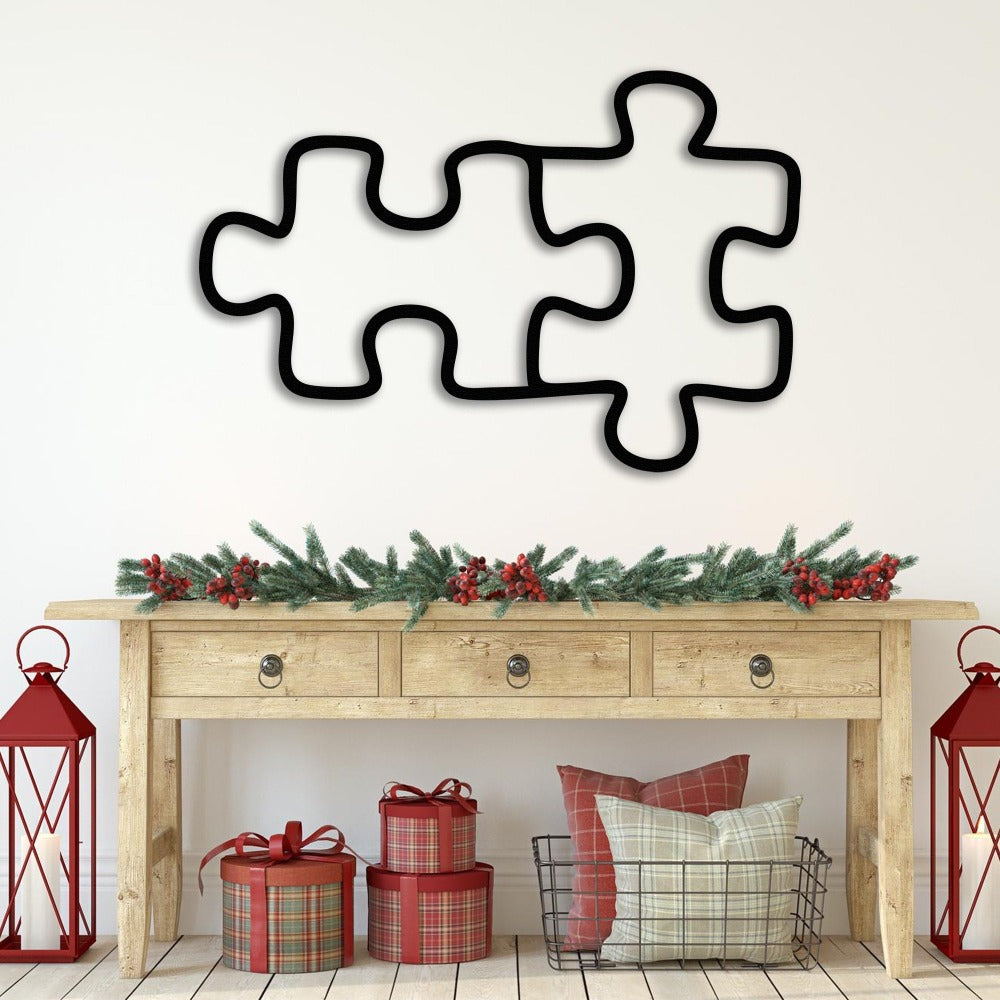 Puzzle piece metal wall art in black placed above a holiday-themed console table with red lanterns, plaid gift boxes, and a greenery garland.