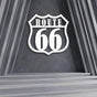 Route 66 metal wall art in white displayed against a modern gray concrete wall with geometric architectural elements, creating a bold and iconic statement piece.