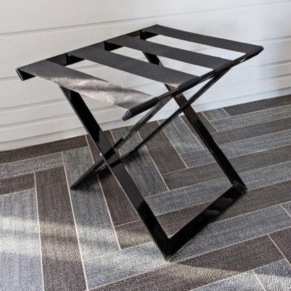  A sleek black foldable luggage rack with metallic finish placed on a modern patterned tile floor, enhancing its aesthetic appeal.