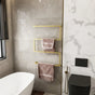 Wall-mounted towel holder on a wall with light grey tiles, holding neatly folded pink towels in an elegant bathroom space.