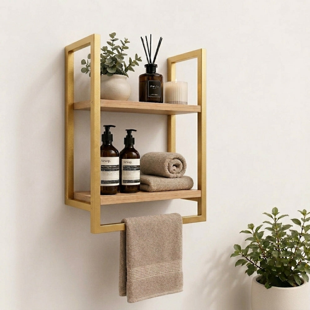 Gold wall mounted 2-tier bathroom shelf with towel bar holding bathroom bottles, towels, and decor.