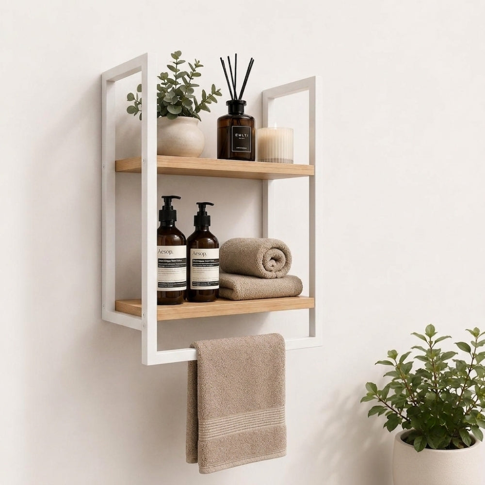 White wall mounted 2-tier bathroom shelf with towel bar holding bathroom bottles, towels, and decor.