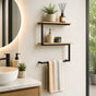 Black wall mounted 2-tier towel shelf with towel bar and wood-look shelves styled beside a bathroom vanity.