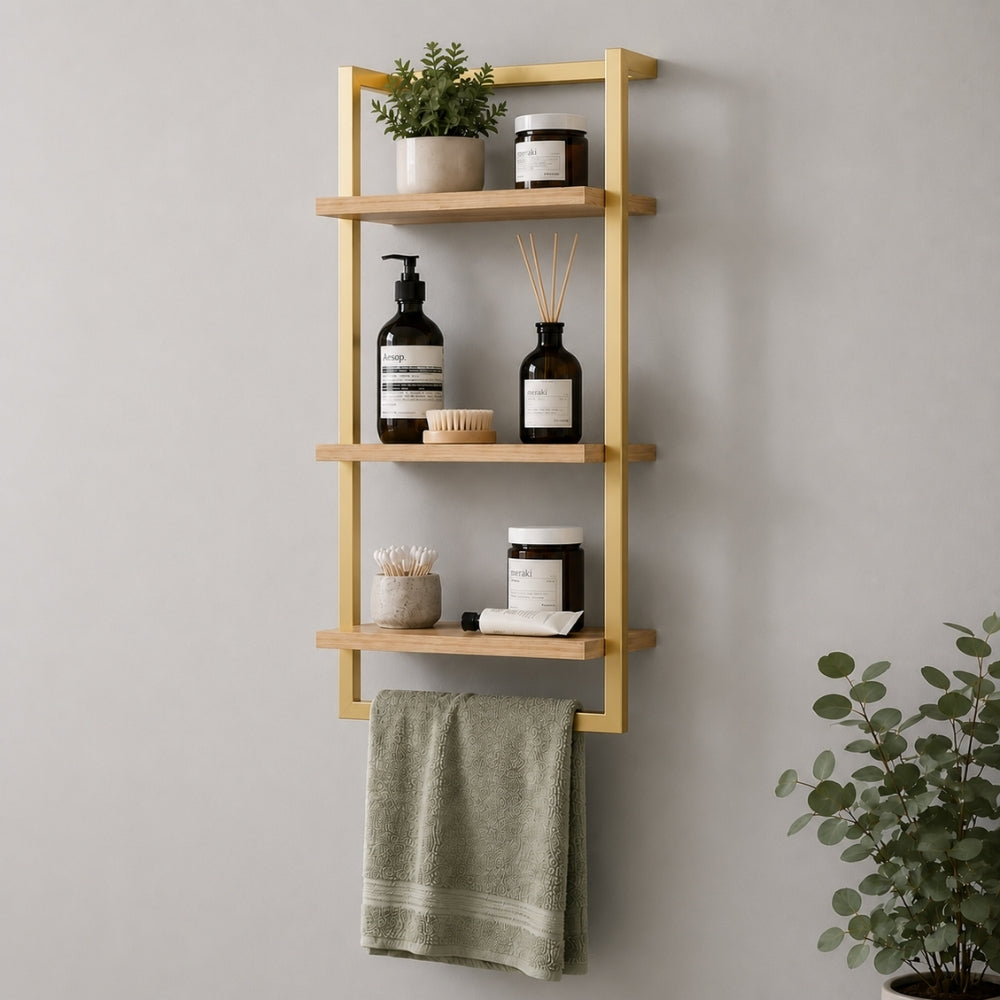 Gold wall mounted 3-tier bathroom shelf with towel bar holding toiletries and a green towel.