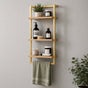 Gold wall mounted 3-tier bathroom shelf with towel bar holding toiletries and a green towel.