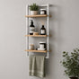 Satin nickel wall mounted 3-tier bathroom shelf with towel bar holding toiletries and a green towel.