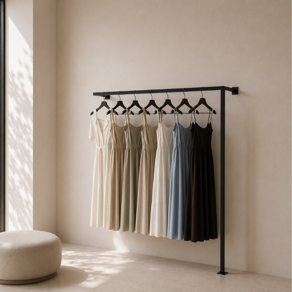 Black wall mounted clothing rack holding dresses in a bright dressing room.