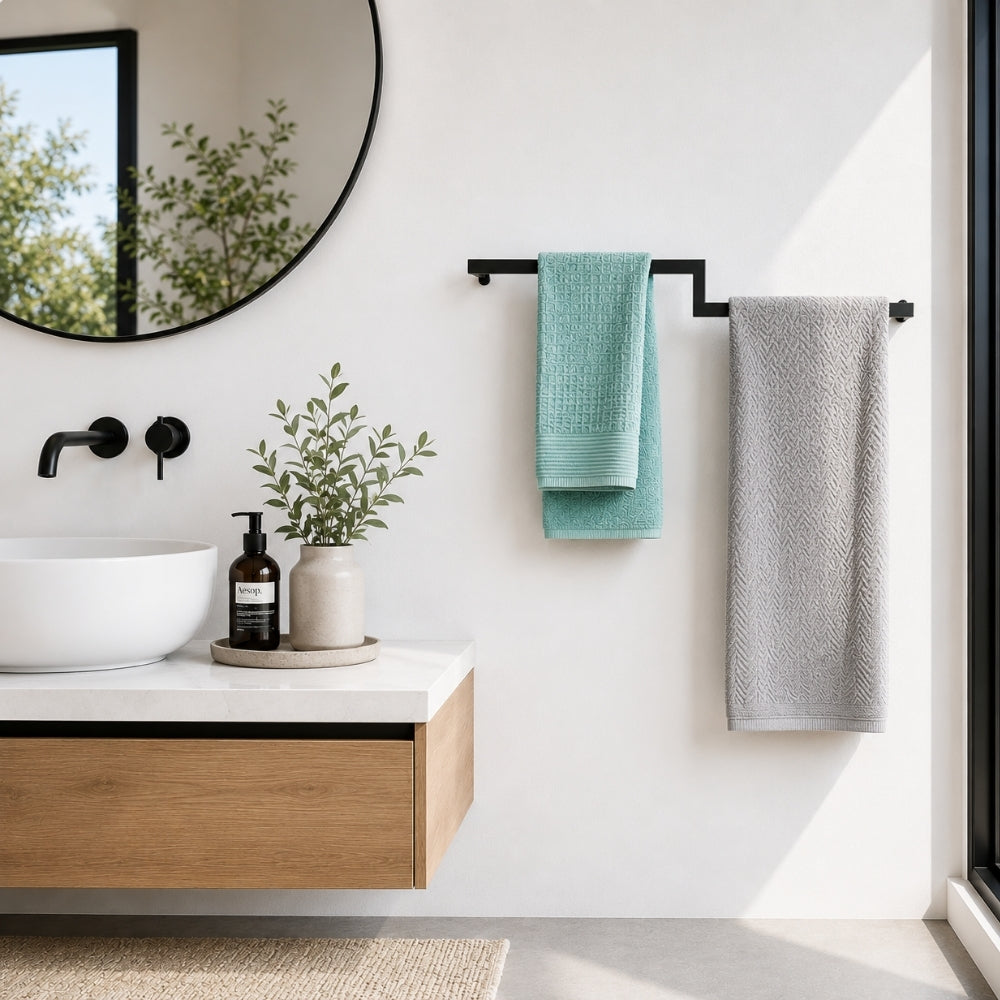 Black wall mounted offset double towel bar holding teal and gray towels beside a modern bathroom vanity.