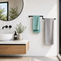 Black wall mounted offset double towel bar holding teal and gray towels beside a modern bathroom vanity.