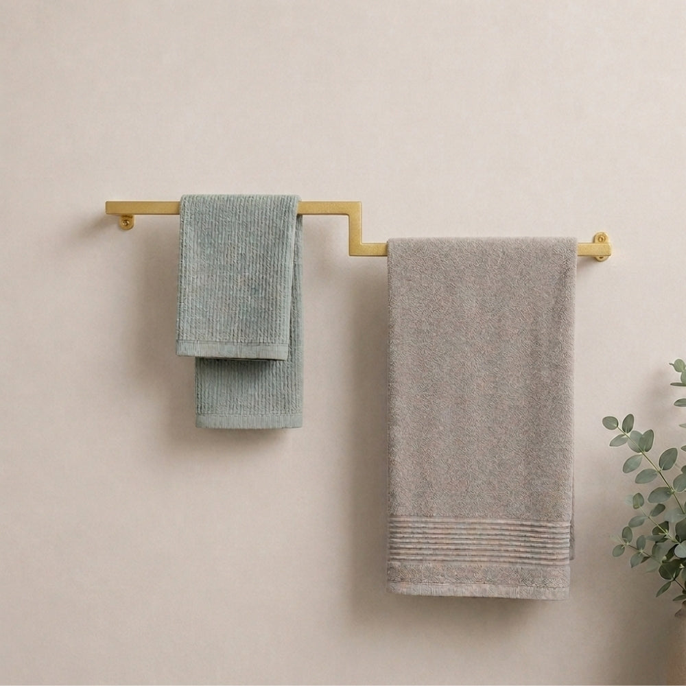 Gold wall mounted offset double towel bar holding mint and gray towels on a bathroom wall.