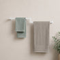 White wall mounted offset double towel bar holding mint and gray towels on a bathroom wall.
