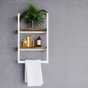 A white wall-mounted bathroom shelf with two wooden shelves and a towel bar, styled with a green plant, amber bottles, and a white towel against a gray tiled wall.